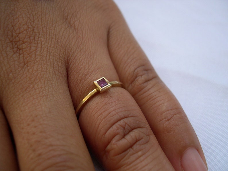 May include: A gold ring with a small square-shaped pink gemstone.