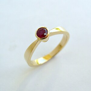 May include: A gold band ring with a single red ruby gemstone set in the center.