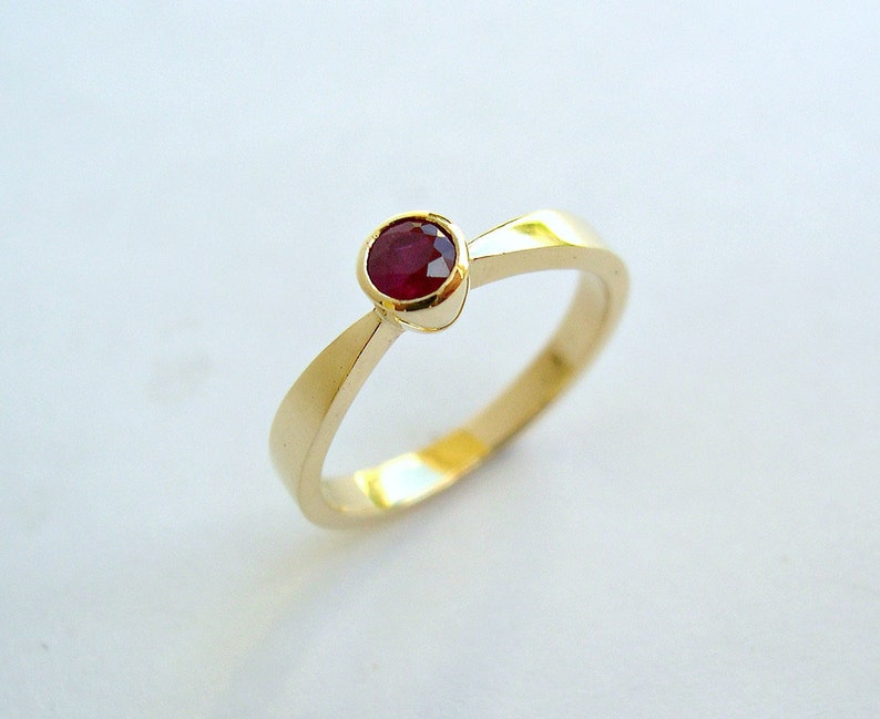 May include: A gold band ring with a single red ruby gemstone set in the center.
