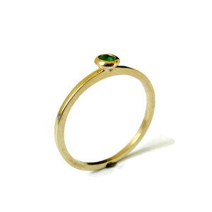 May include: A simple gold band ring with a small green gemstone set in the center.