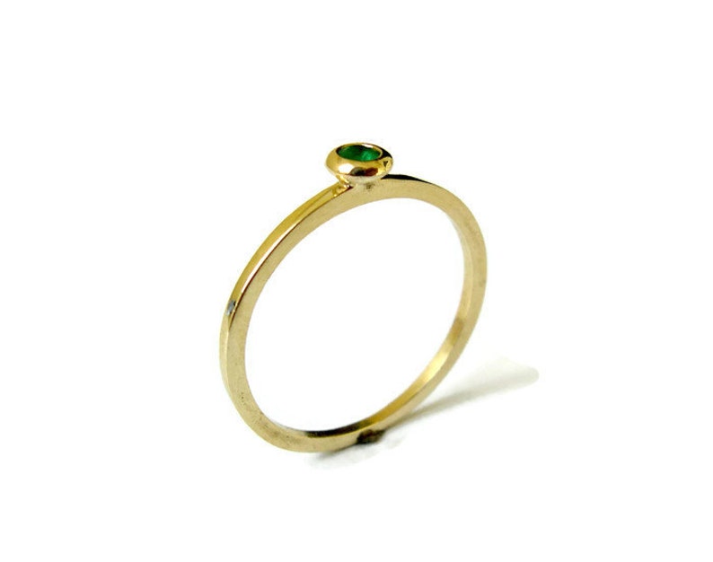 May include: A simple gold band ring with a small green gemstone set in the center.