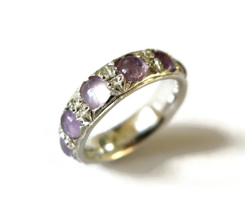 May include: A silver band ring with five purple gemstones set in a floral design.