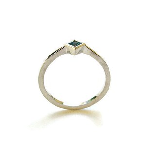 Puede incluir: Un anillo de plata con una pequeña piedra preciosa azul cuadrada engastada en el centro.