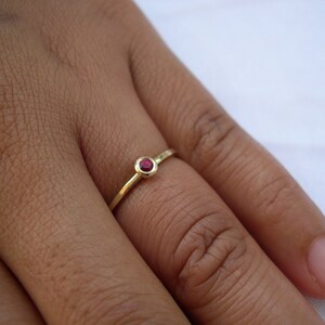 May include: A simple gold band ring with a small, round, red gemstone.