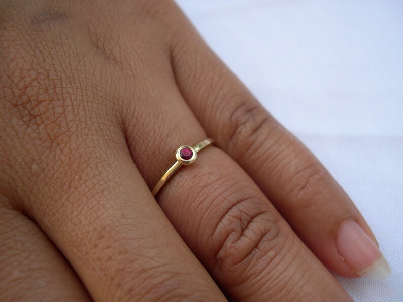 May include: A simple gold band ring with a small, round, red gemstone.