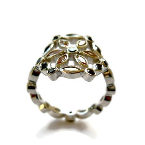 Puede incluir: Un anillo de plata con un dise&ntilde;o floral con piedras preciosas negras y transparentes. El anillo est&aacute; hecho de metal y tiene un dise&ntilde;o delicado e intrincado.