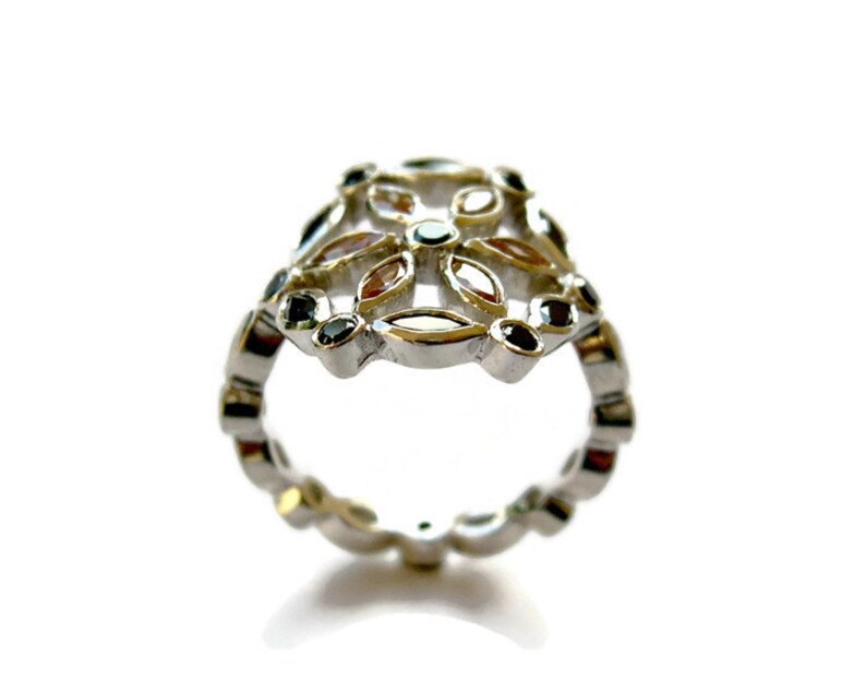 Puede incluir: Un anillo de plata con un dise&ntilde;o floral con piedras preciosas negras y transparentes. El anillo est&aacute; hecho de metal y tiene un dise&ntilde;o delicado e intrincado.