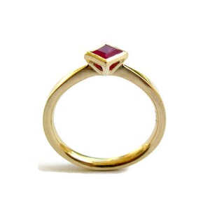 May include: A gold ring with a red square-shaped gemstone set in a geometric design.