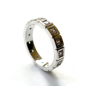 Puede incluir: Un anillo de banda de plata con una fila de pequeños diamantes de forma cuadrada engastados en la banda.