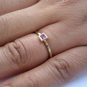 May include: A gold ring with a small, square, pink gemstone set in the center.