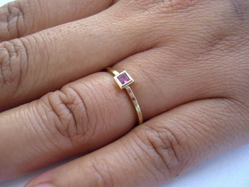 May include: A gold ring with a small, square, pink gemstone set in the center.