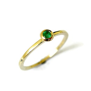 May include: A simple gold band ring with a small, round emerald green gemstone set in the center.