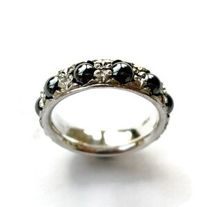 Puede incluir: Un anillo de banda de plata con piedras preciosas negras engastadas en un diseño floral.