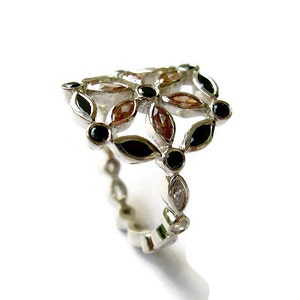 Puede incluir: Un anillo de plata con un dise&ntilde;o floral con piedras preciosas negras y marrones.