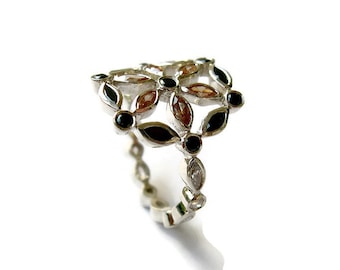 Puede incluir: Un anillo de plata con un diseño floral con piedras preciosas negras y marrones.