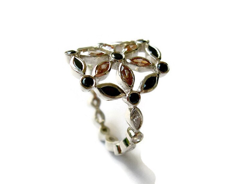 Puede incluir: Un anillo de plata con un dise&ntilde;o floral con piedras preciosas negras y marrones.