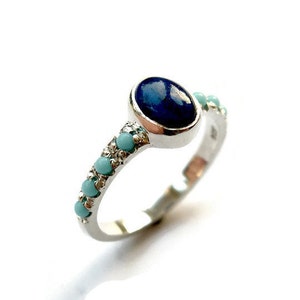 Puede incluir: Un anillo de plata con una piedra ovalada azul oscuro y una banda de cuentas azules claras.
