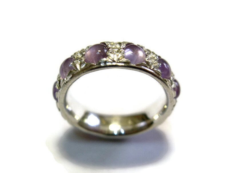 May include: A silver band ring with a row of purple gemstones and smaller clear gemstones.
