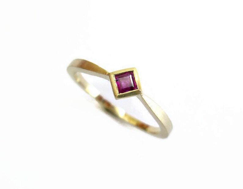 May include: A gold ring with a small, square, pink gemstone set in the center.