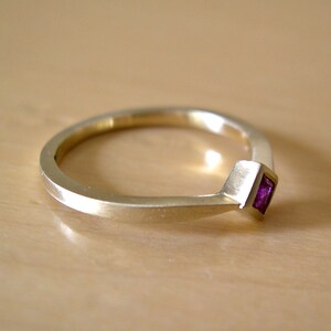May include: A gold band ring with a small, square, purple gemstone set in the center.
