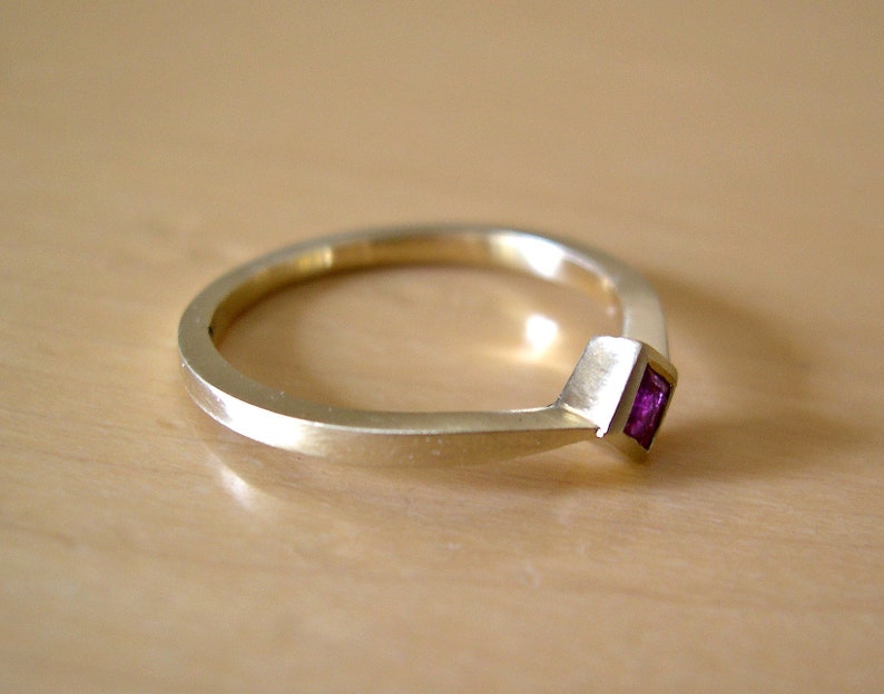May include: A gold band ring with a small, square, purple gemstone set in the center.