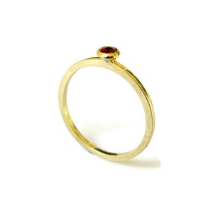 May include: A simple gold band ring with a single red gemstone set in the centre.