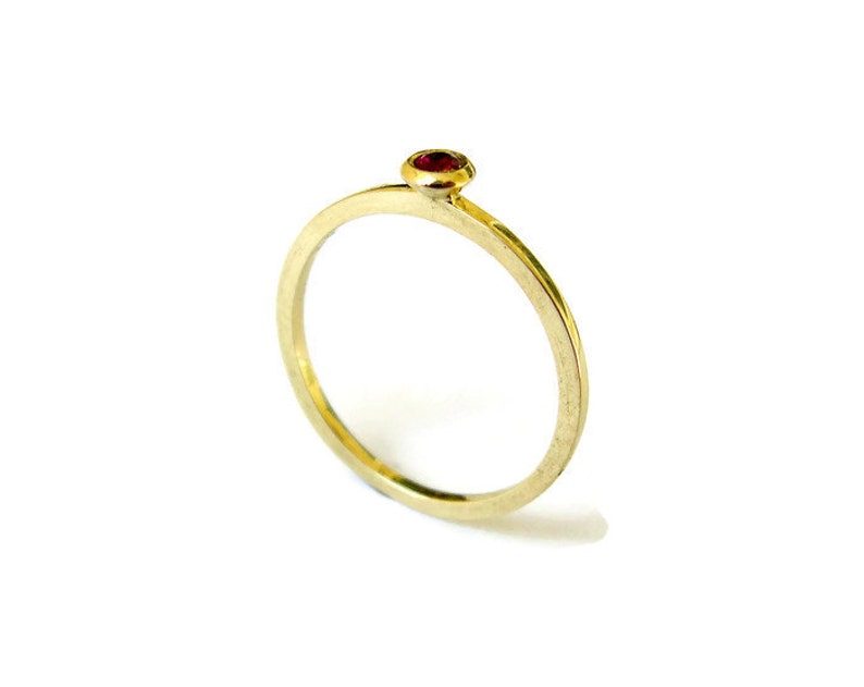 May include: A simple gold band ring with a single red gemstone set in the centre.