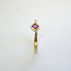 May include: A gold ring with a square-shaped ruby gemstone.