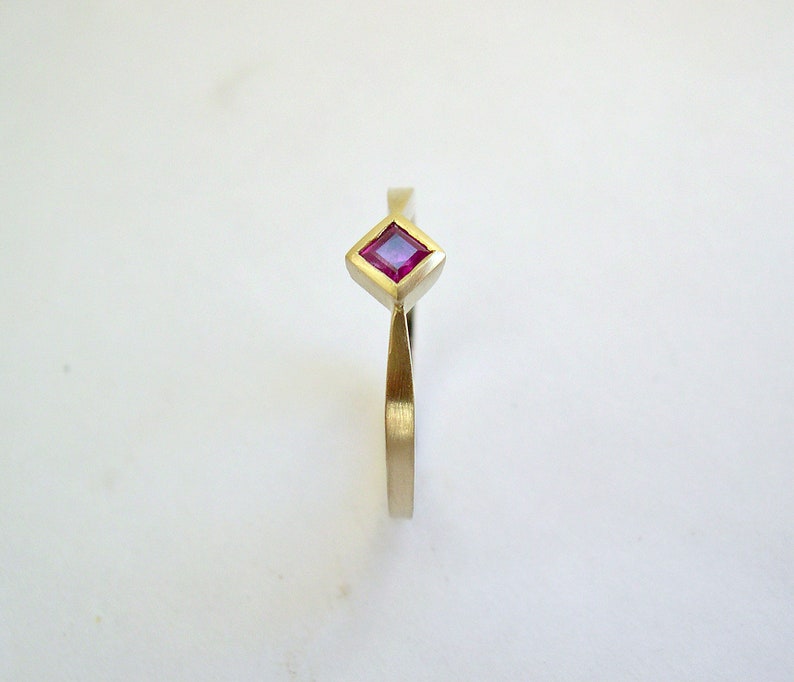 May include: A gold ring with a square-shaped ruby gemstone.