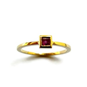 May include: A gold ring with a small square-shaped ruby gemstone set in the center.