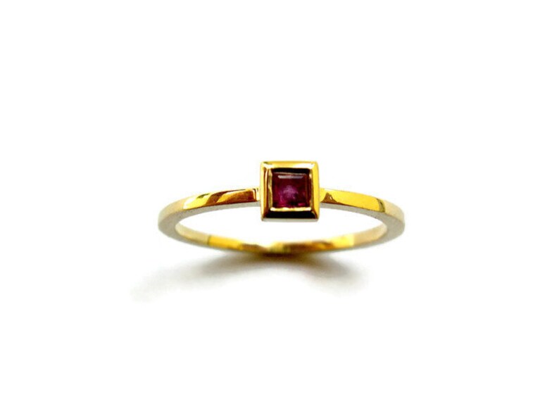 May include: A gold ring with a small square-shaped ruby gemstone set in the center.