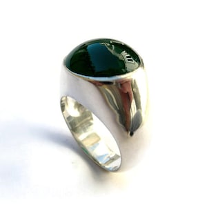 Puede incluir: Un anillo de plata con una gran piedra preciosa redonda de color verde oscuro.