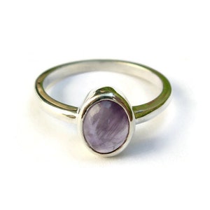 May include: A silver ring with a light purple oval gemstone set in a bezel setting.