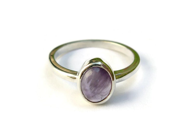 May include: A silver ring with a light purple oval gemstone set in a bezel setting.