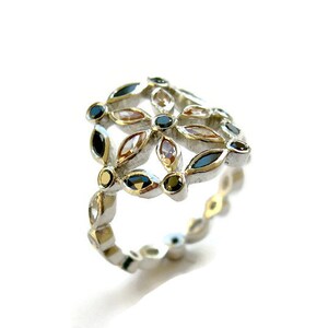 Puede incluir: Un anillo de plata con un dise&ntilde;o floral con piedras preciosas negras, blancas y doradas.