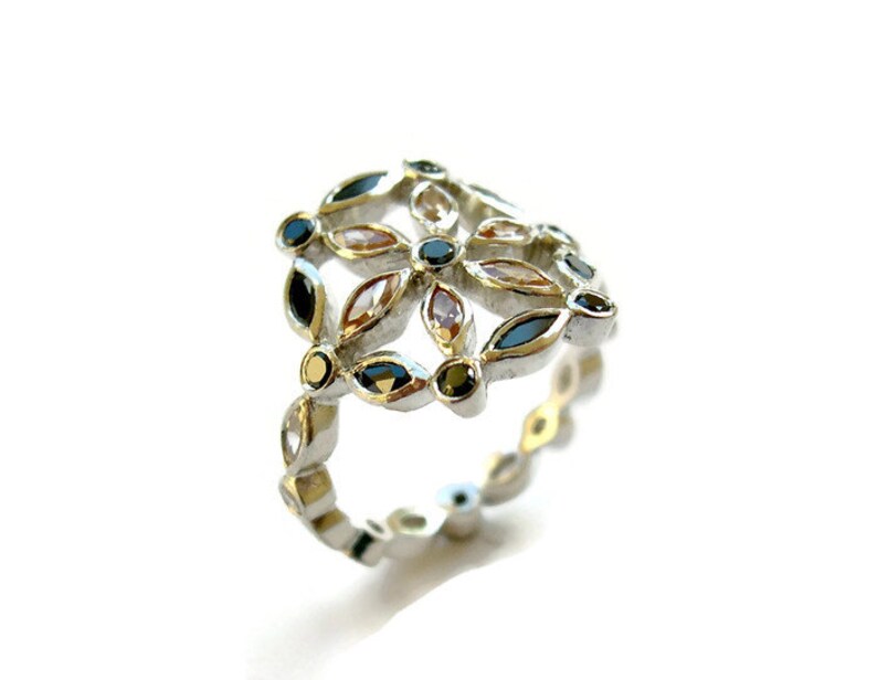 Puede incluir: Un anillo de plata con un dise&ntilde;o floral con piedras preciosas negras, blancas y doradas.