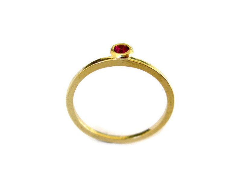 May include: A simple gold band ring with a single red gemstone set in the centre.
