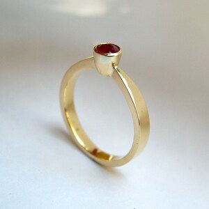 May include: A simple gold band ring with a single red gemstone set in a bezel setting.