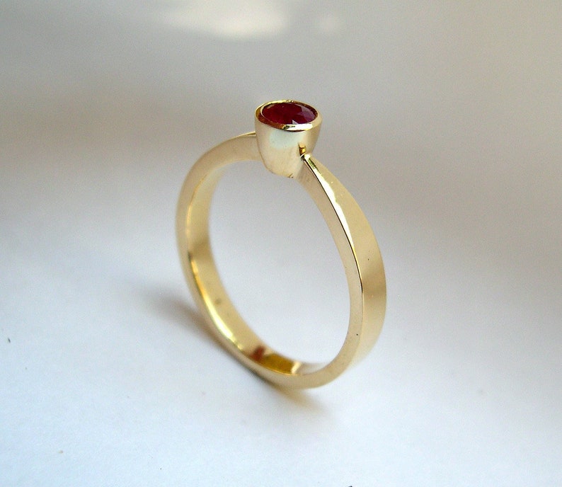 May include: A simple gold band ring with a single red gemstone set in a bezel setting.