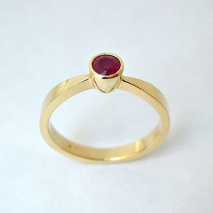 May include: A simple gold band ring with a single red ruby gemstone set in the center.