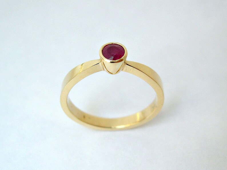 May include: A simple gold band ring with a single red ruby gemstone set in the center.
