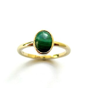 Puede incluir: Un anillo de oro con una piedra ovalada de malaquita verde.