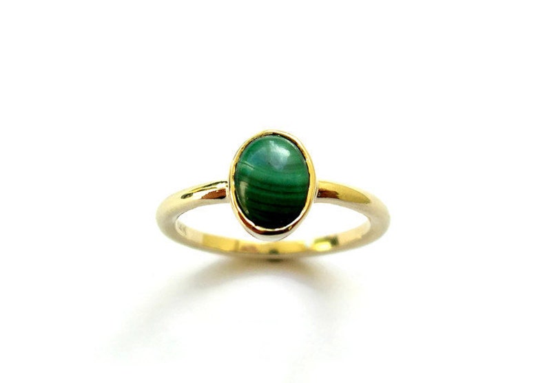 Puede incluir: Un anillo de oro con una piedra ovalada de malaquita verde.