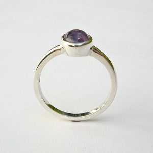 May include: A silver ring with a purple gemstone set in a bezel setting.