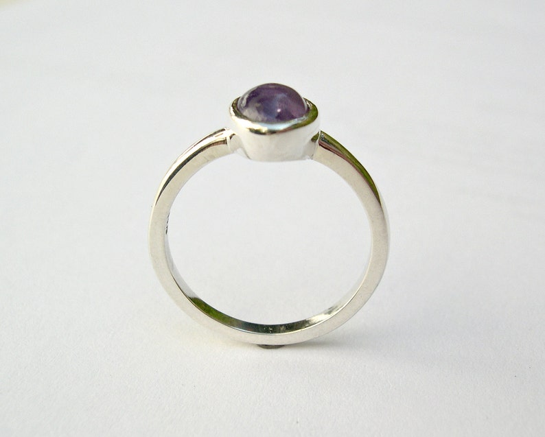 May include: A silver ring with a purple gemstone set in a bezel setting.
