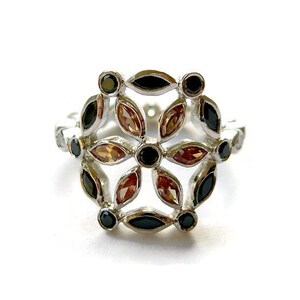 Puede incluir: Un anillo de plata con un dise&ntilde;o floral con piedras preciosas negras y marrones.