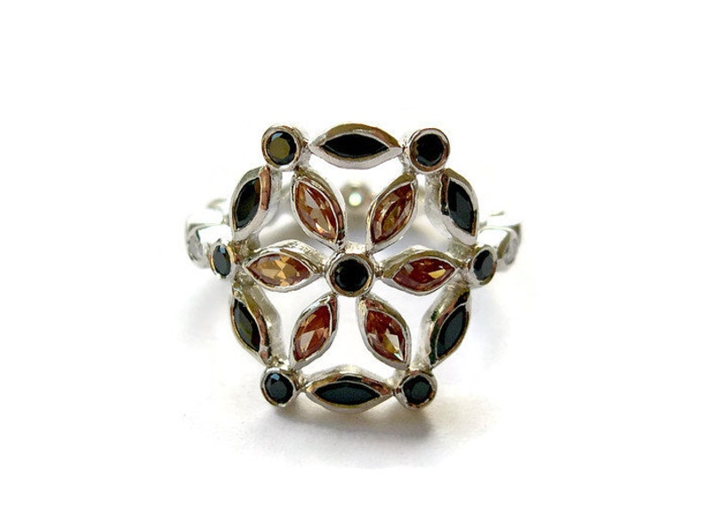 Puede incluir: Un anillo de plata con un dise&ntilde;o floral con piedras preciosas negras y marrones.