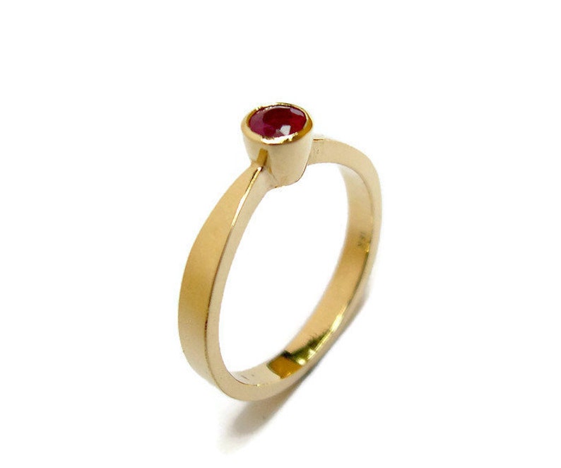 May include: A simple gold band ring with a single red gemstone.