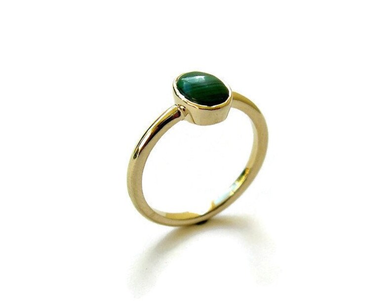 Puede incluir: Un anillo de oro con una piedra preciosa ovalada verde. El anillo es simple y elegante.