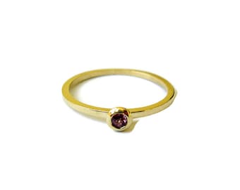 May include: A simple gold band ring with a single small pink gemstone set in the center.
